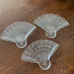 Peut inclure: Trois plats en verre transparent en forme d'éventail avec un motif décoratif. Les plats sont disposés sur une surface en bois.