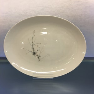 May include: An oval, white serving platter with a delicate floral design in shades of gray and pink. The platter is made of porcelain and has a glossy finish. The floral design is on the left side of the platter.
