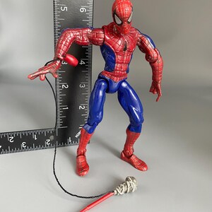 May include: A red and blue Spider-Man action figure with a web shooter accessory. The figure is posed in a dynamic action stance with one leg forward and one arm extended.