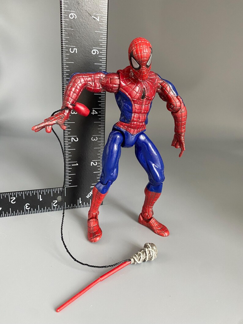 May include: A red and blue Spider-Man action figure with a web shooter accessory. The figure is posed in a dynamic action stance with one leg forward and one arm extended.