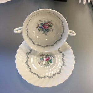 Peut inclure: Une tasse à thé et une soucoupe en porcelaine blanche avec un motif floral. La tasse a un bord festonné et une anse. La soucoupe a un bord festonné et un motif floral autour du bord.