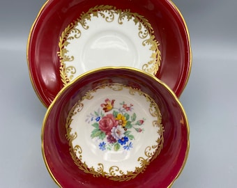 May include: A vintage teacup and saucer set. The cup and saucer are a deep red with gold trim. The interior of the cup and the center of the saucer are white with a floral design. The handle of the cup is gold.