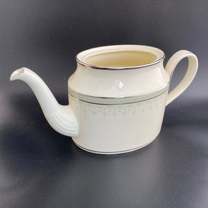May include: A white ceramic teapot with a silver rim and a green floral design. The teapot has a spout and a handle.