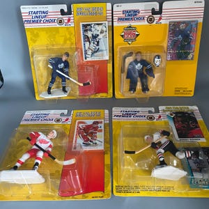 May include: Four hockey player action figures in packaging. The figures are dressed in their team uniforms and holding hockey sticks. The packaging is yellow and features the NHL logo. The figures are from the 1995 edition of the Starting Lineup series.