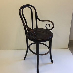 May include: A black wooden chair with a curved back and arms. The chair has a brown leather seat and a round footrest.