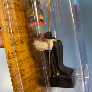 Peut inclure: Une petite figurine d&eacute;taill&eacute;e d'un pharaon &eacute;gyptien assis sur un tr&ocirc;ne, tenant un b&acirc;ton. La figurine est peinte en or, noir, vert et rouge.