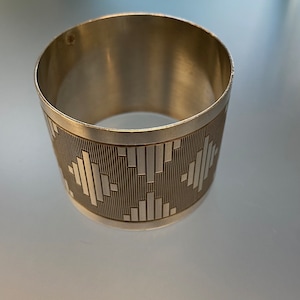 May include: Silver napkin ring with a geometric design. The ring is made of polished silver and has a simple, modern design.