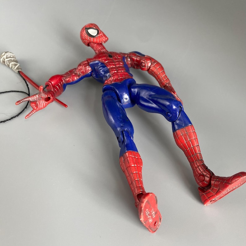 May include: A red and blue plastic action figure of Spider-Man with web shooters. The figure is posed with one arm outstretched and the other bent at the elbow. The figure is wearing a red and blue suit with a spider logo on the chest.