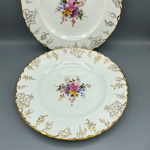 Peut inclure: Deux assiettes en porcelaine blanche avec des bordures dorées et des motifs floraux. Les assiettes ont un bord festonné et un motif de vigne.