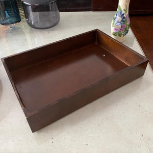 Könnte beinhalten: Ein rechteckiges, dunkelbraunes Holztablett mit glänzender Oberfläche. Das Tablett ist leer und hat ein schlichtes, klassisches Design. Das Tablett wird wahrscheinlich zum Servieren oder Aufbewahren verwendet.