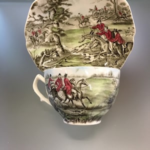 Puede incluir: Un juego de té vintage de taza y platillo con un diseño de escena de caza. El juego presenta un fondo verde y marrón con jinetes vestidos de rojo a caballo y perros que persiguen a un zorro.