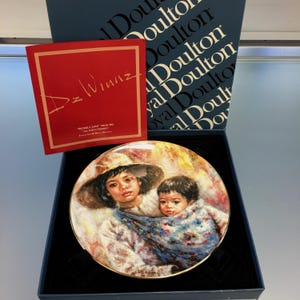 Peut inclure: Une assiette de collection Royal Doulton représentant une peinture d'une femme portant un enfant. L'assiette est dans une boîte bleue avec le logo Royal Doulton. L'assiette est intitulée "Sisterly Love" de la collection "All God's Children" de l'artiste De Winne.