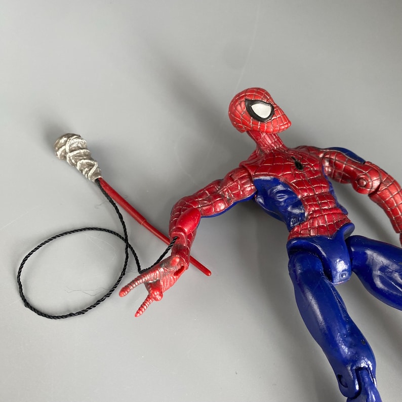 May include: A red and blue action figure of Spider-Man with a web shooter accessory. The figure has a detailed design and is posed in a dynamic action pose.