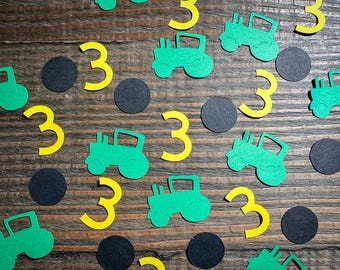 May include: Green and yellow paper cutouts of tractors and the number three on a wood background. The cutouts are scattered across the surface.