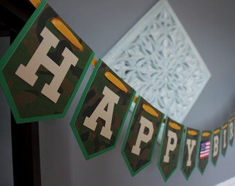 May include: A green and brown camouflage patterned banner with the words "Happy Birthday" in white letters. The banner is strung together with yellow ribbon.