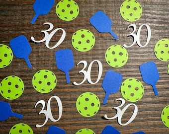 May include: A collection of green and blue paper cutouts on a wooden background. The cutouts include paddles, balls, and the number 30.