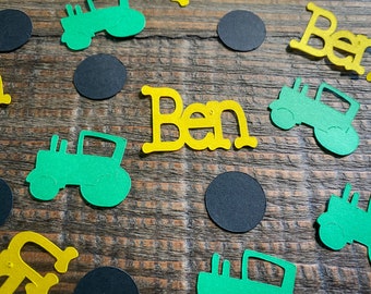 May include: Green and yellow paper cutouts of tractors and the name Ben on a wood background. The cutouts are scattered on the wood surface.