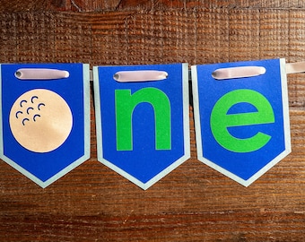 May include: A blue and white banner with the word "one" in green letters. The first letter is replaced with a golf ball.