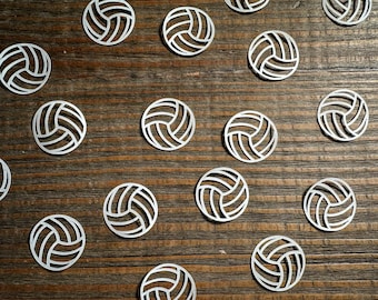 Könnte beinhalten: Eine Holzoberfläche mit mehreren silbernen Volleyball-Ausschnitten, die darauf verstreut sind.