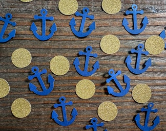 Puede incluir: Confetti de ancla azul y confetti de purpurina dorado sobre una superficie de madera. Las anclas son de varios tamaños y el confetti de purpurina es redondo.