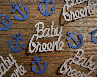 Puede incluir: Confetti de purpurina plateado con el texto "Baby Greene" y confetti de papel azul en forma de ancla.
