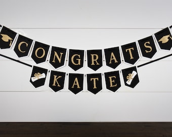 Pode incluir: Faixa de graduação preta e dourada com o texto "Congrats Kate" e ícones de chapéu de formatura e diploma.