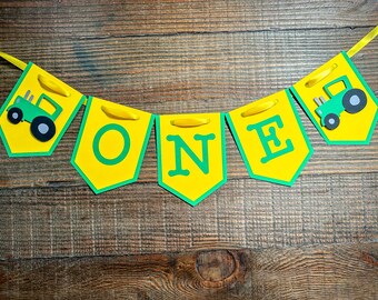 Puede incluir: Una pancarta amarilla y verde con la palabra "ONE" en letras verdes y dos tractores de juguete verdes en cada extremo.