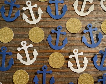 Puede incluir: Una colección de confeti de ancla de color azul marino y blanco con círculos de purpurina dorada. Las ancras están recortadas en papel y tienen un diseño sencillo.