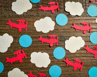 Pode incluir: Aviões de papel vermelhos e nuvens de papel brancas com círculos de papel azuis sobre um fundo de madeira. Esses recortes de papel são perfeitos para um chá de bebê ou uma festa de aniversário.
