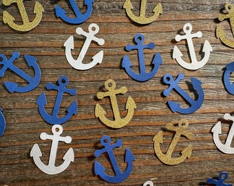 Puede incluir: Una colección de confeti de ancla de color dorado, blanco y azul. Las ancras están hechas de papel y tienen un acabado brillante.