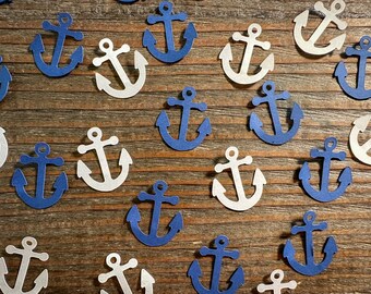 May include: A collection of blue and white paper anchor cutouts. The anchors are scattered on a wooden surface.