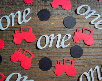 May include: Red and white paper confetti with the word "one" in white and tractor cutouts. The background is a woodgrain surface.