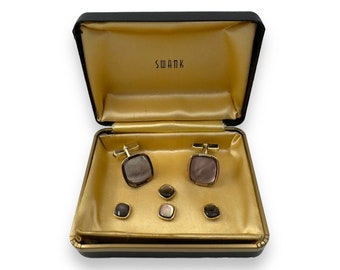 May include: A set of cufflinks and studs in a black box with a gold interior. The cufflinks and studs are made of gold metal and have a mother-of-pearl inlay. The box has the word "SWANK" printed on the inside of the lid.
