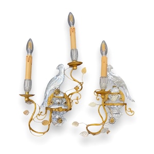 Puede incluir: Un par de apliques de pared doradas con detalles de pájaros de cristal y candelabros de vidrio transparente. Cada aplique tiene dos candelabros y un pájaro de cristal posado en una rama.