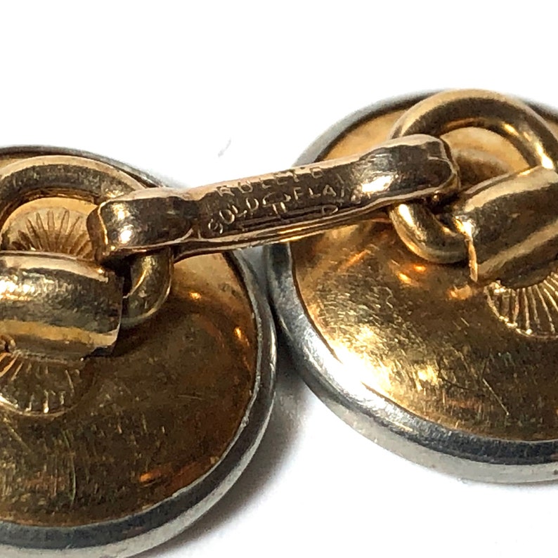Puede incluir: Un par de gemelos chapados en oro con respaldo de plata. Los gemelos tienen un dise&ntilde;o circular y las palabras "Gold Plated" est&aacute;n grabadas en la barra de conexi&oacute;n.