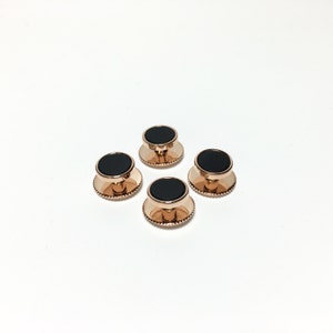May include: Set of four black and rose gold cufflinks. Each cufflink has a round black center and a rose gold rim with a beaded edge.