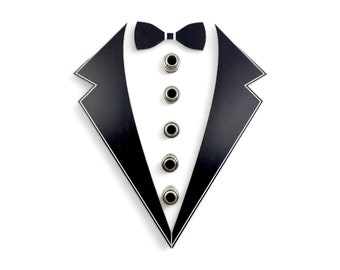 May include: A black tuxedo cutout with five silver buttons down the front and a black bow tie at the top.