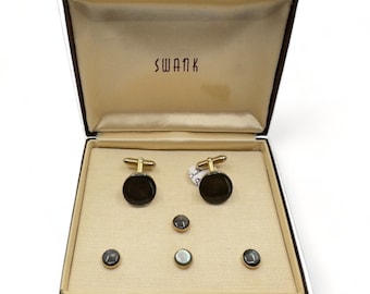May include: A black Swank cufflinks and stud set in a brown box. The cufflinks and studs are made of black mother of pearl and gold metal.