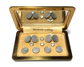 May include: A gold-coloured box with a mirrored lid, containing a set of 10 mother-of-pearl cufflinks and studs. The box is labelled "Krementz - Stag".
