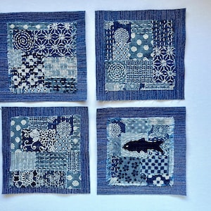 May include: Four square denim patches with intricate patterns and stitching in shades of blue and white. One patch features a black fish silhouette. The patches are arranged on a white surface.