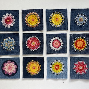 May include: Twelve square denim fabric patches arranged in a grid, each featuring a unique, circular, multi-colored floral embroidery design. The embroidery uses vibrant threads in shades of yellow, red, pink, blue, and white to create intricate patterns.