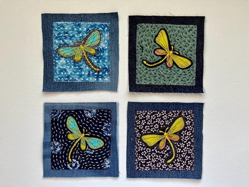 May include: Four square fabric patches with dragonfly designs. Each patch features a denim border and a central design of a dragonfly in shades of yellow, blue, and black. The backgrounds vary with patterns of blue, green, and white.