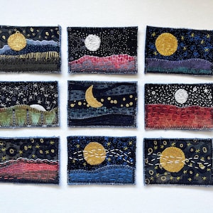 May include: Nine rectangular fabric patches arranged in a grid, each featuring hand-embroidered night sky scenes. The designs include various moons, stars, and landscapes in colors like gold, white, red, blue, and green on dark backgrounds.
