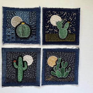 May include: Four square fabric patches with embroidered cactus designs. Each patch features a different cactus, a moon, and a dark blue background with white stitching. The patches have a frayed denim border.