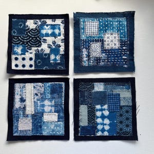 May include: Four square indigo-dyed fabric patches with various patterns and textures. Each patch is a unique combination of blue and white fabrics, showcasing different designs and stitching techniques. The patches are framed with a dark blue border.