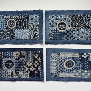 May include: Four rectangular denim patches with intricate, hand-stitched designs in shades of blue and white. Each patch features a unique pattern, including circles, waves, and floral motifs, showcasing the artistry of Japanese sashiko embroidery.