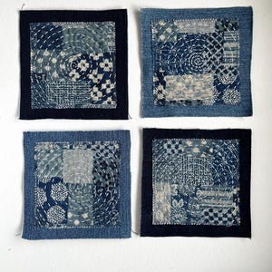 May include: Four square textile patches with indigo blue and white patterns. Each patch features a unique design, including concentric circles and geometric shapes, with visible white stitching. Two patches have a dark blue border.