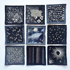 May include: A set of nine square fabric patches arranged in a grid. Each patch features a dark blue denim border surrounding a central square of patterned fabric, including designs with stars, moons, dragonflies, leaves, and geometric motifs.