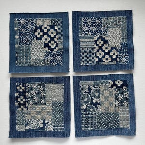 May include: Four square denim patches with intricate, hand-stitched designs in shades of blue and white. Each patch features a unique combination of geometric and floral patterns, showcasing the artistry of the stitching.