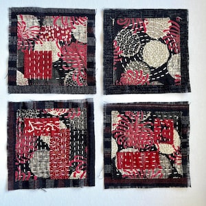 May include: Four square fabric patches with a patchwork design. Each patch features a dark blue plaid border, with red, black, and beige patterned fabric inside. White stitching accents the design, creating a textured appearance. The patches are arranged on a white background.